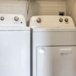 The James Apartments | Laundry room with a matching white Whirlpool washer and dryer set under a wire shelf | Luxury Apartments in Haverhill MA