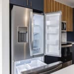 The James Apartments | Kitchen with an open stainless steel refrigerator, showing a well-organized space with adjacent dark blue and wooden cabinetry | Luxury Apartments in Haverhill MA