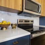 The James Apartments | Close-up of a modern kitchen stove and microwave with custom tile backsplash and decorative accents including a bowl of lemons and a brass bowl on the countertop | Luxury Apartments in Haverhill MA