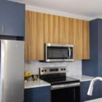 The James Apartments | Stainless Steel Modern kitchen with stainless steel appliances, including a double-door refrigerator and microwave, accented by dark blue and wooden cabinetry | Luxury Apartments in Haverhill MA