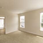 The James Apartments | Bedroom with beige carpet, multiple windows, and a door leading to a hallway with wooden flooring | Luxury Apartments in Haverhill MA