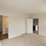 The James Apartments | Bedroom with beige carpet, multiple doors leading to a bathroom and hallway, and bright natural light from windows | Luxury Apartments in Haverhill MA