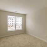 The James Apartments | Empty bedroom with beige carpet and a large window, offering a view of the exterior construction site | Luxury Apartments in Haverhill MA