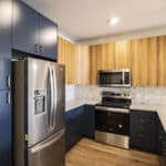 The James Apartments | Close-up of a modern kitchen featuring wooden upper cabinets, navy lower cabinets, stainless steel appliances, and white quartz countertops | Luxury Apartments in Haverhill MA