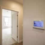 The James Apartments | Smart home ADT system panel mounted on the wall near a doorway, leading to a carpeted bedroom with natural light | Luxury Apartments in Haverhill MA