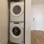 The James Apartments | Stacked white washer and dryer units in a compact laundry closet with wood-style flooring | Luxury Apartments in Haverhill MA